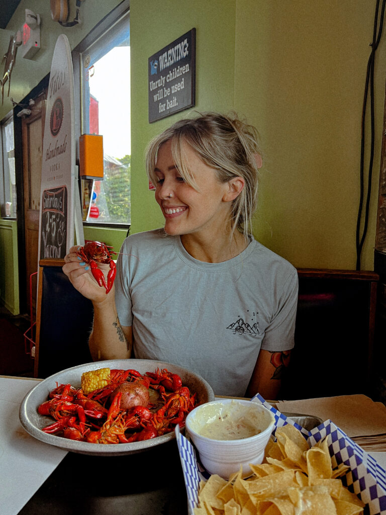 Blonde girl enjoying a crawfish meal at a restaurant in Austin, Texas, with a bib on and a pile of crawfish on a plate in front of her.